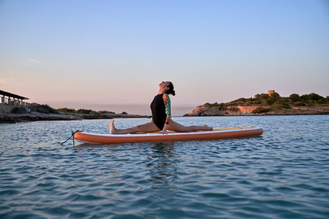 Sporty female athlete taking Front Splits pose on SUP board