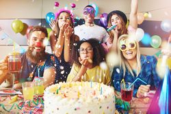 Friends smiling surrounding a birthday cake with confetti and streamers