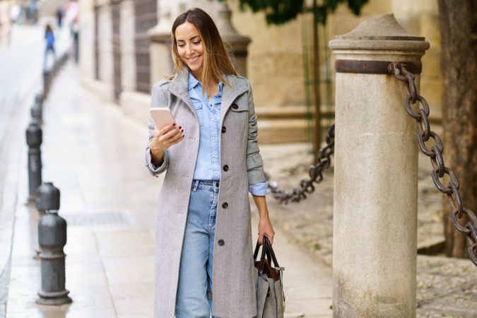 Woman in coat using smartphone on street