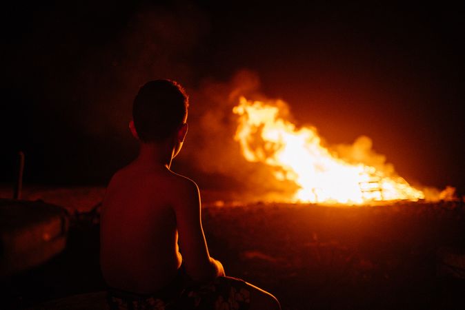 Back of young boy watching fire in field