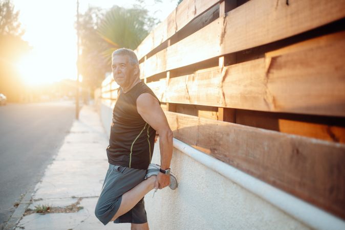 Mature man stretching on wooden wall in street