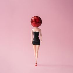 Barbie like doll in dark dress with red disco ball head with pink background