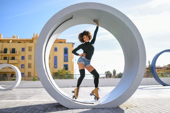 Woman wearing roller-skates posing while standing inside circular outdoor sculpture