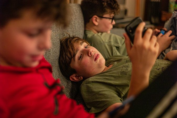 Three boys using their phone and sitting on couch