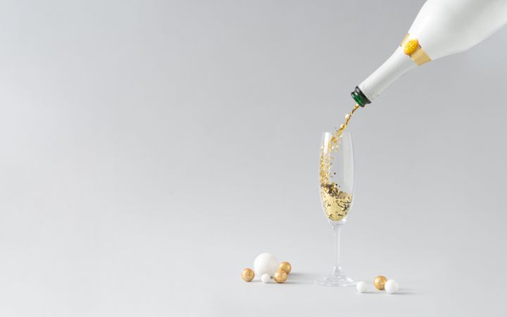 Champagne bottle pouring golden glitter into the glass on light background