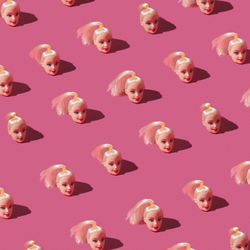 Pattern made of doll heads on pink background