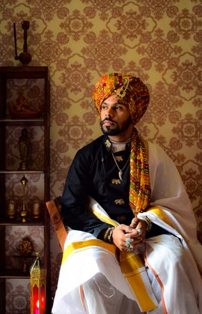Man turban and traditional outfit sitting on chair indoor