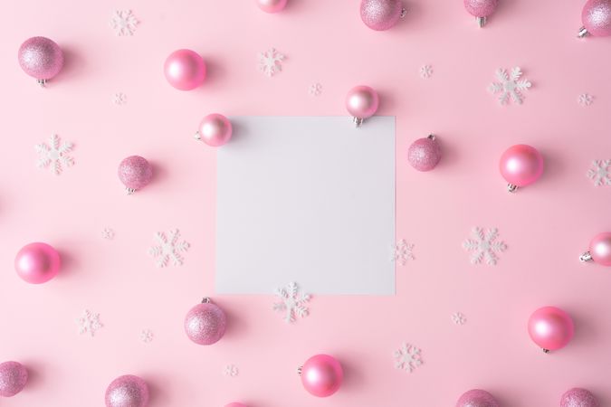 Different shades of pink baubles and snowflakes on a pink background with paper card