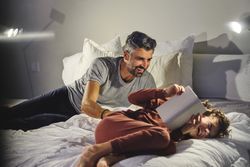Father tickling son on bed