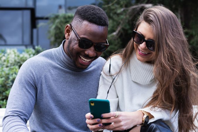 Joyful multiethnic couple listening music on smartphone in park