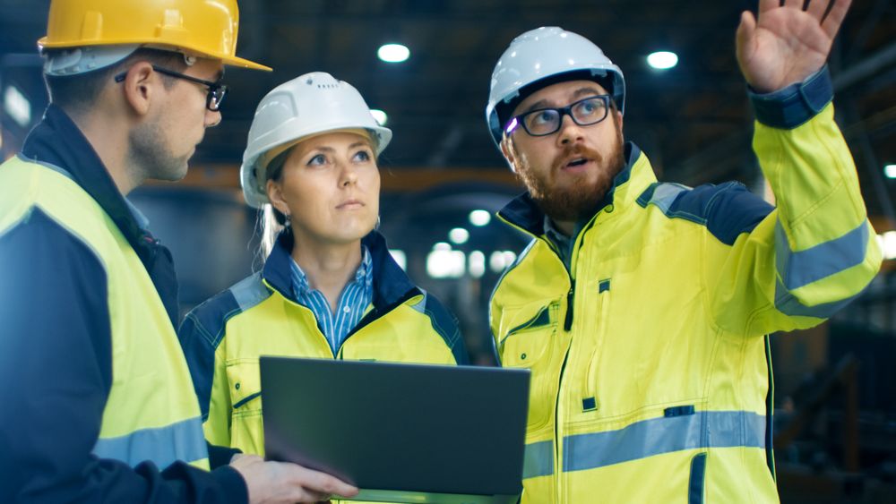 Male and Female Industrial Engineers Talk with Factory Worker while Using Laptop.