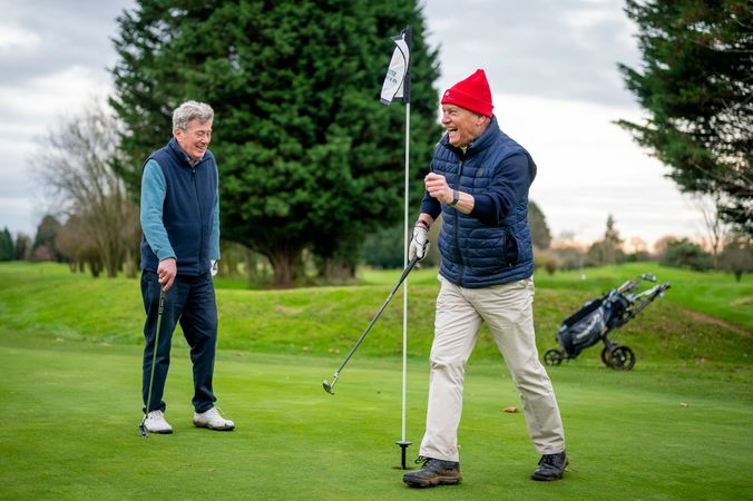 Mature male friends celebrating good shot on golf course