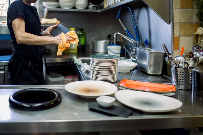 Crop woman cleaning plates in kitchen