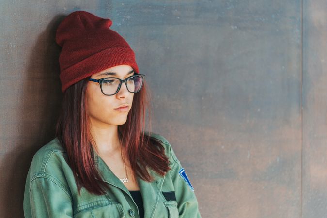 Stylish confident woman in glass and hat leaning on wall and looking away