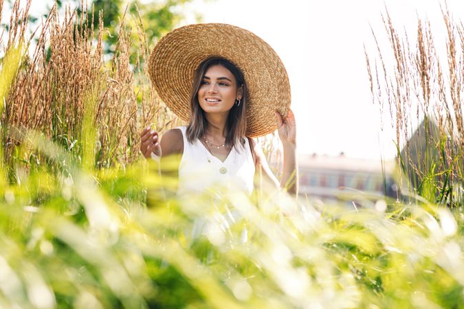Calm woman in straw hat standing outside in pond grass