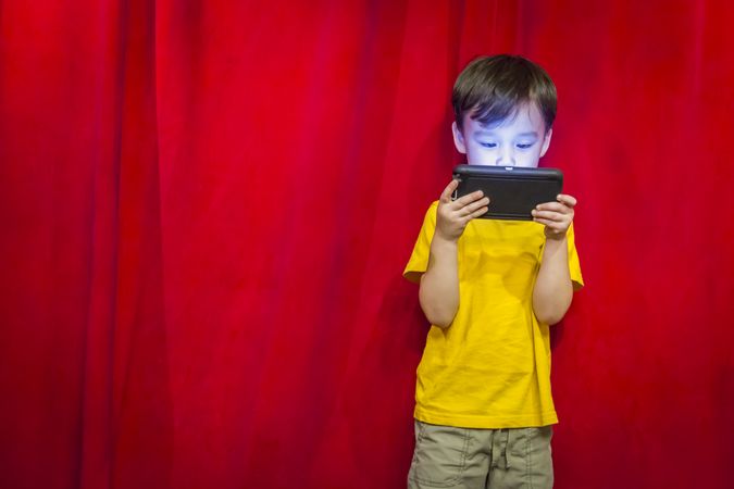 Biracial Boy Watching Cell Phone in Front of Curtain