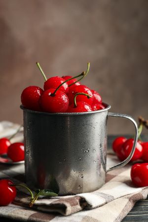 Towel and metal mug with cherry on wooden background. Summer plant