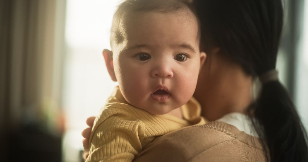 Portrait of a Cute Asian Baby Resting in the Embrace of her Mother, While She Gently Caresses her Back.