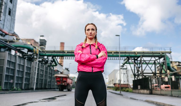 Sportswoman with crossed arms posing in front of a factory