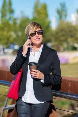 Woman standing outside talking on phone holding a to go coffee