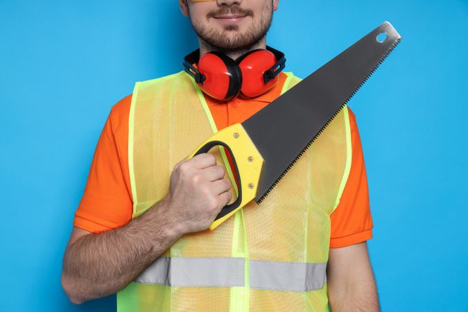 Engineer with saw in hands on blue background, space for text