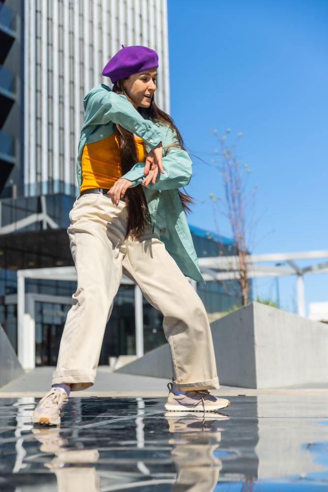 Young Asian Woman In Colorful Outfit Dancing On Urban Water Feature With Modern Buildings In Background