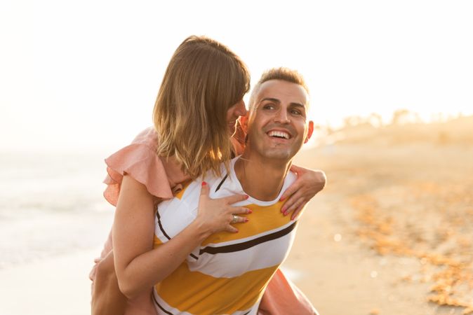 Man carrying woman on back near sea