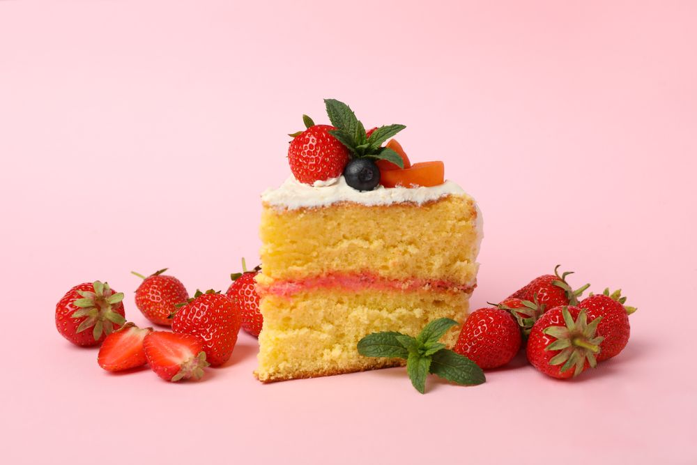 Piece of berry cream cake on pink background. Delicious dessert