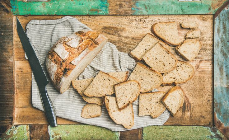 Homemade loaf with slices arranged in line with serrated knife, on green trimmed wooden board