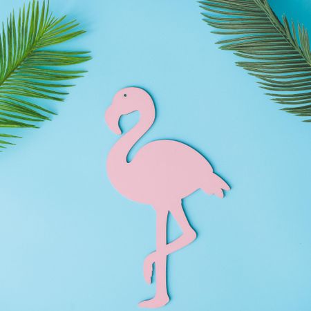 Pink flamingo shape with green tropical leaves on bright blue background