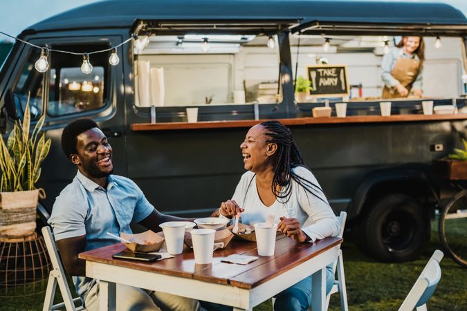Happy black couple laughing during dinner near food truck