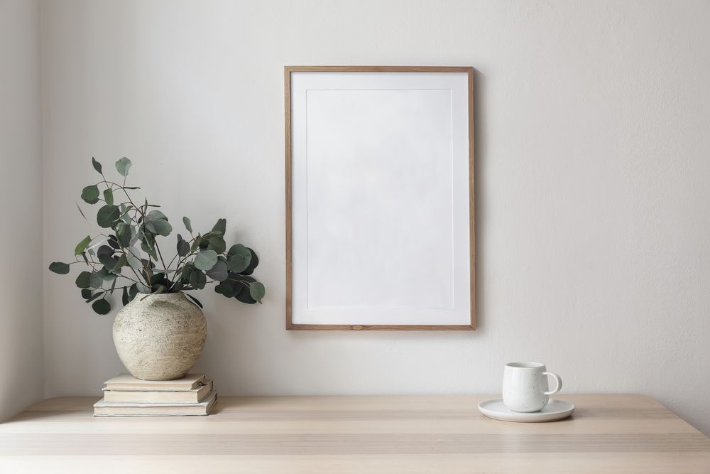 Minimal breakfast still life cup of coffee, tea, empty wall in sunlight table, vase with silver eucalyptus leaves, branches on old books with mock up poster