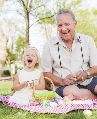 Grandfather and Granddaughter Coloring Easter Eggs on Blanket At Park