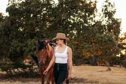 Young woman in hat walking with her horse in the countryside at sunset