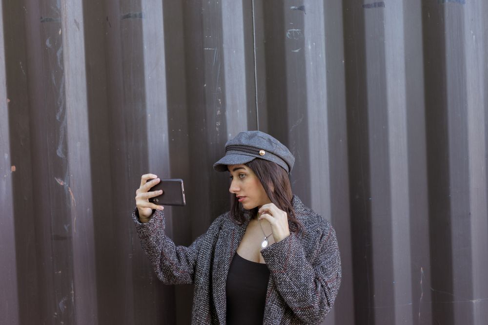 Charming Hispanic lady taking selfie near wall