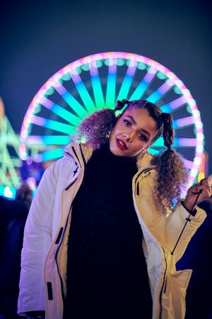 Young woman standing in front of Ferris wheel lit at night