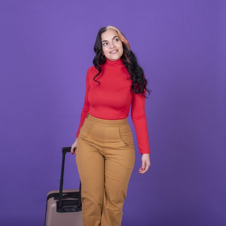 woman traveler holding her suitcase while walking against purple background.