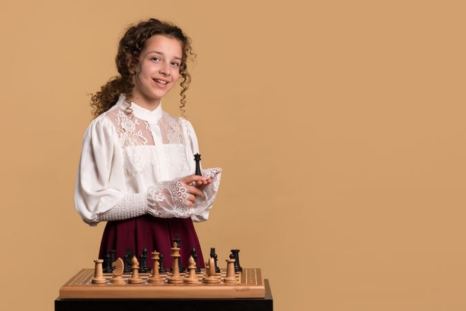 Young girl smiling while holding chess piece in hand.