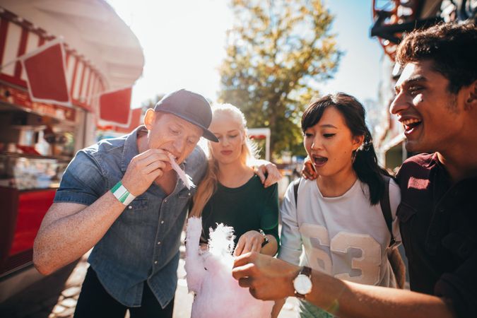 Group of friends eating cotton candy together in amusement park