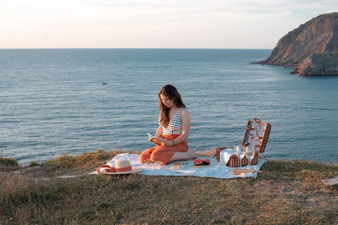 Woman reading on mat for picnic on seashore