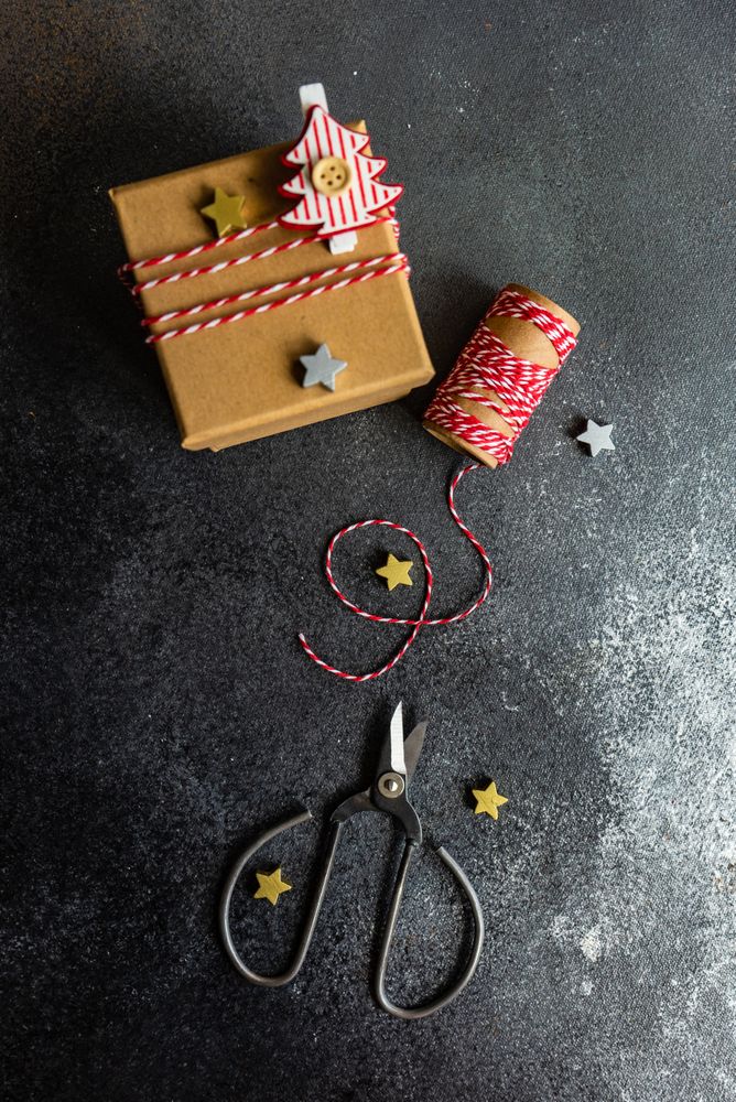 Top view of brown Christmas present with tree decoration, scissors and string