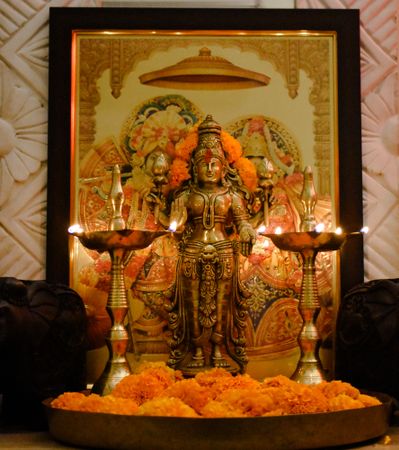 Lakshmi Hindu goddess golden statue between Diyas on marigold flower