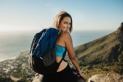 Hiking woman stops near lake in mountains, carries backback, holds thermos  of hot beverage, explores Stock Photo by wayhomestudioo