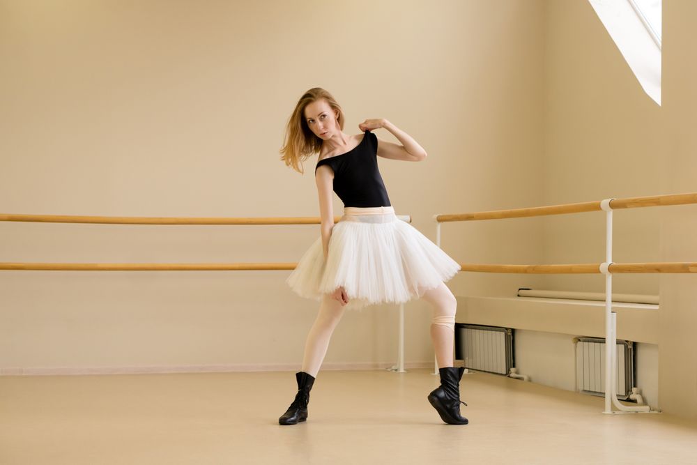 Ballerina in shoes and tutu, holding shoulder in modern dance
