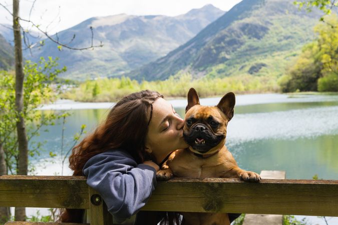 Female traveler kissing dog near lake in mountains