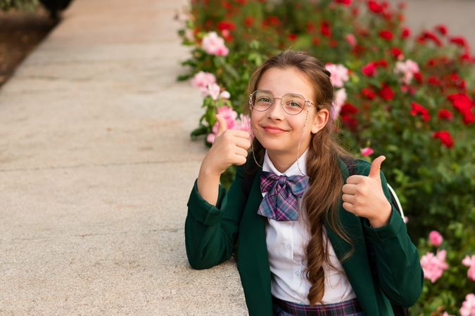 Girl in uniform giving thumbs up while leaning against ledge