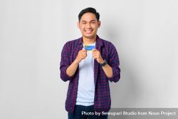 Asian male in grey studio holding up credit card with his hands 5n9ql0