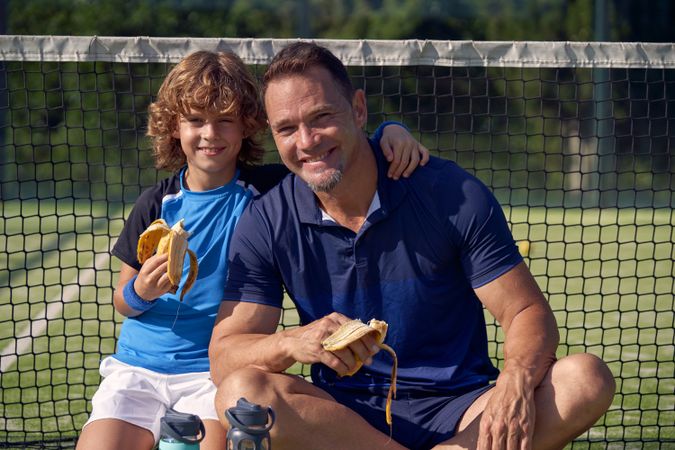 Smiling boy and trainer with bananas on court
