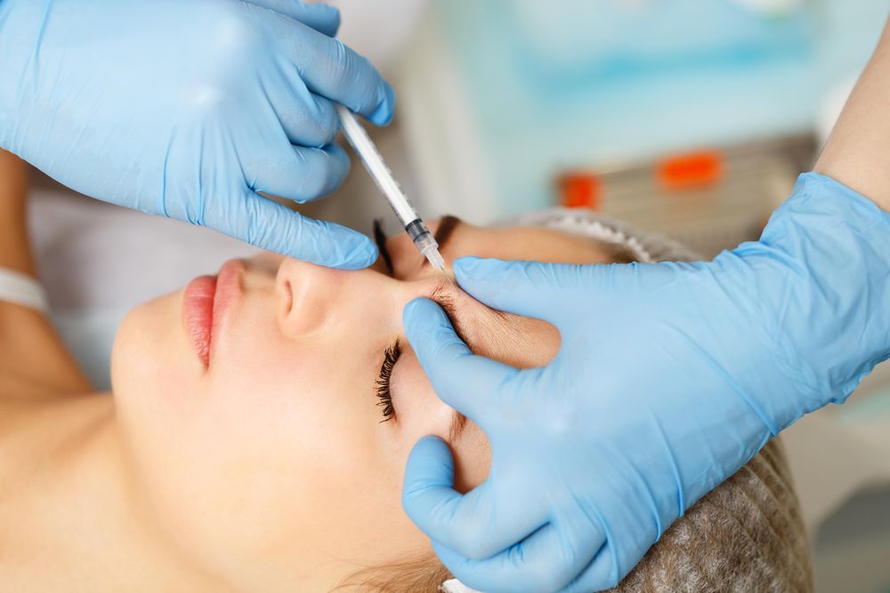 Hands in latex gloves injecting botox into forehead wrinkles in female client