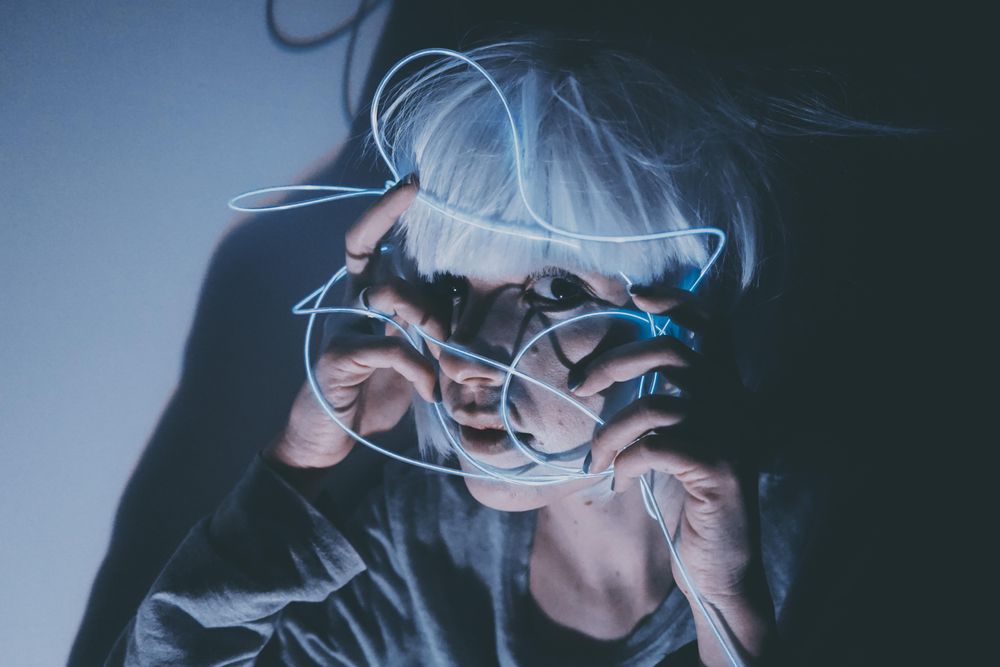 Portrait of woman with light hair holding blue led light thread to her face